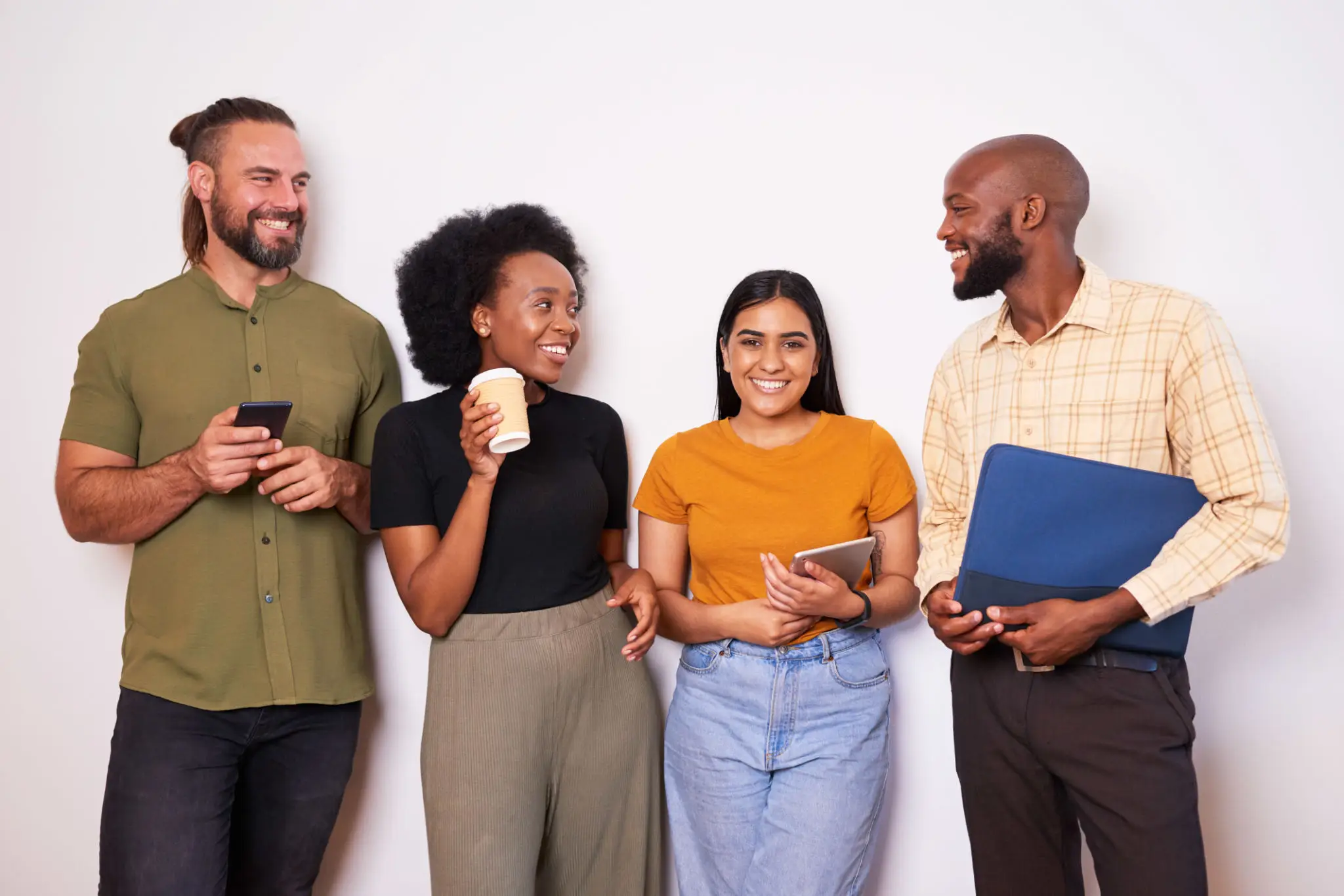 Four people standing and smiling with devices. Four people standing and smiling with devices.
