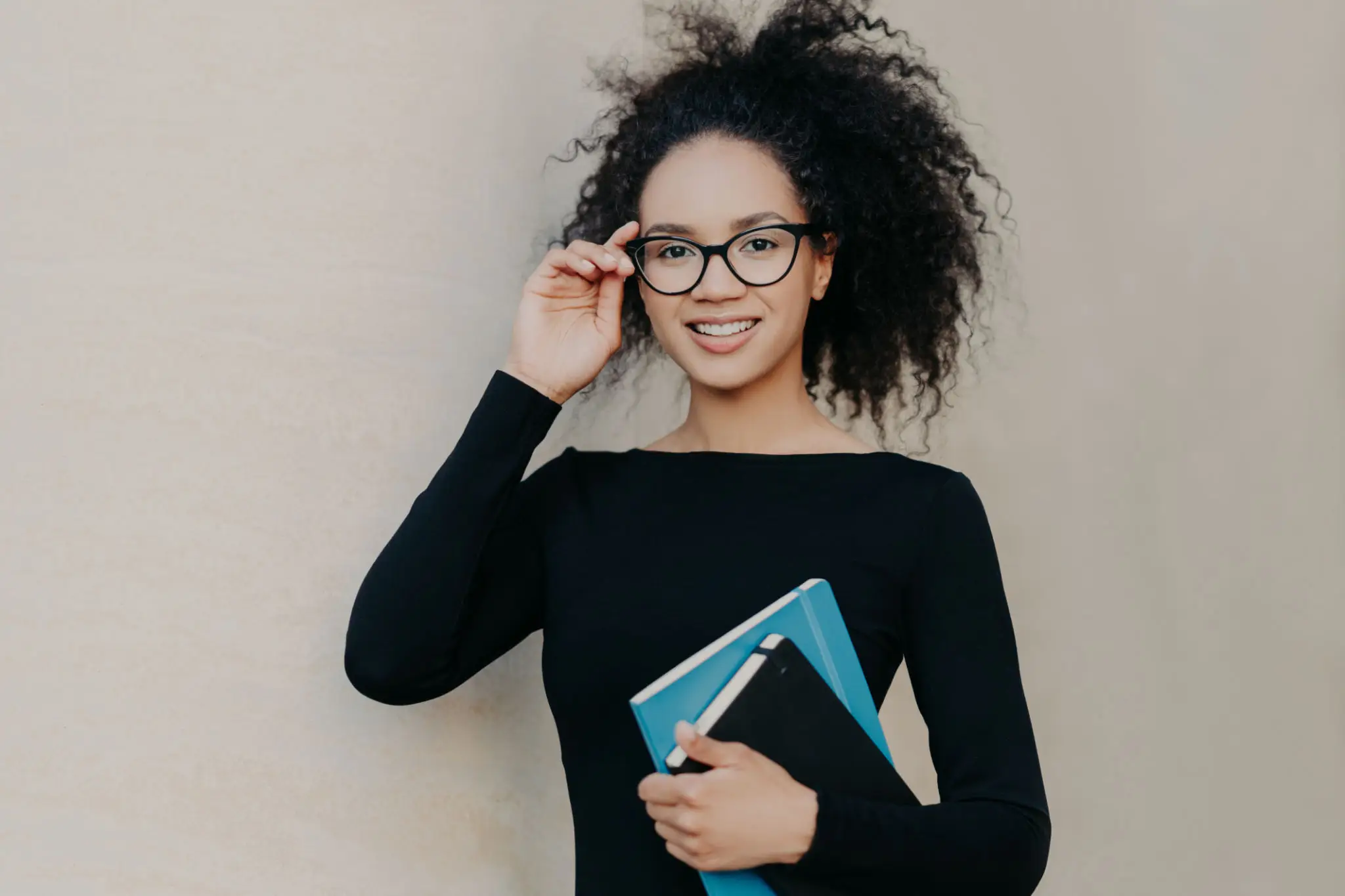 Woman with glasses holding a notebook, smiling. Woman with glasses holding a notebook, smiling.