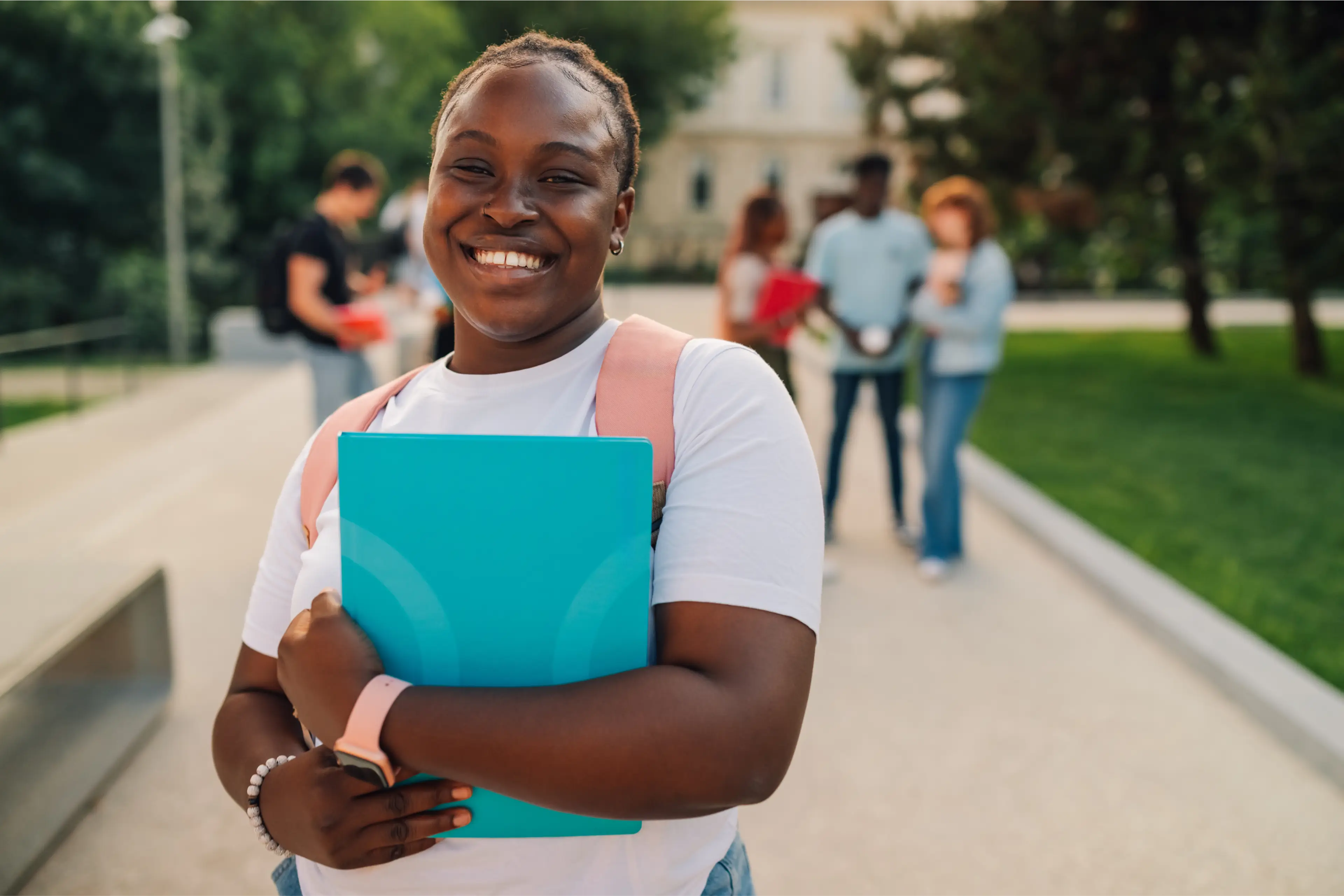 Student smiling with folder, standing outdoors. Student smiling with folder, standing outdoors.