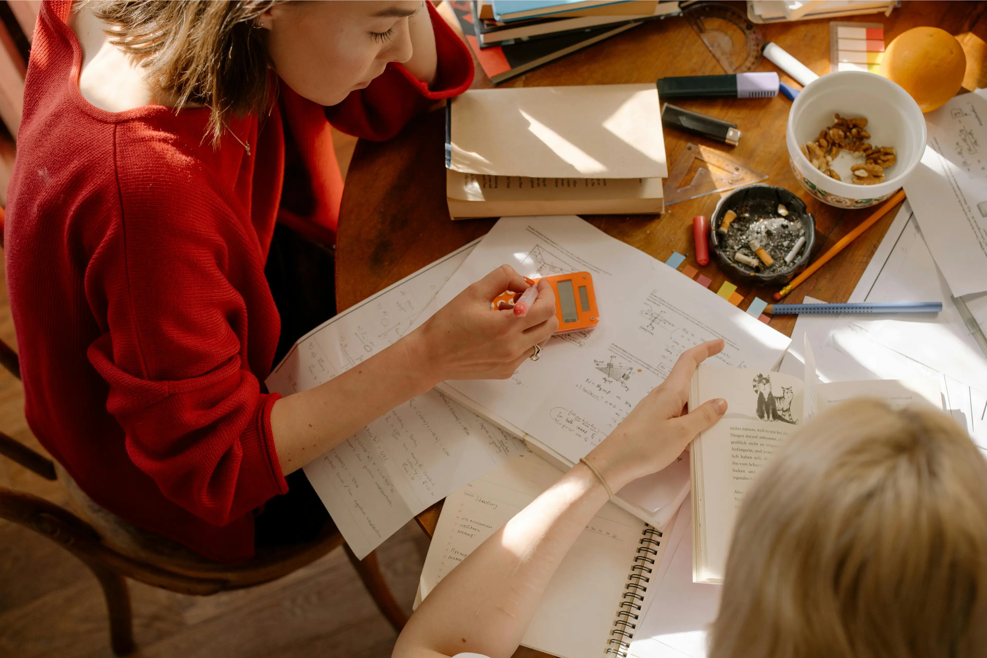 Two people studying at a cluttered table. Two people studying at a cluttered table.